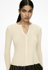 Hellbeige, langärmlige Strickjacke aus strukturiertem Netzgewebe, mit V-Ausschnitt und Knopfverschlüssen vorne.
