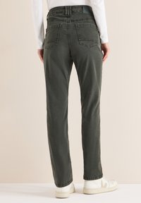 Ciemnozielone dżinsy o luźnym kroju, z dwoma tylnymi kieszeniami i lekko znoszoną fakturą. Połączone z białymi sneakersami.