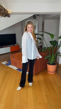 Chemise blanche à manches longues avec boutons et poignets, associée à un pantalon noir à jambes larges. Tissu doux à la texture lisse, portée avec des ballerines blanches.