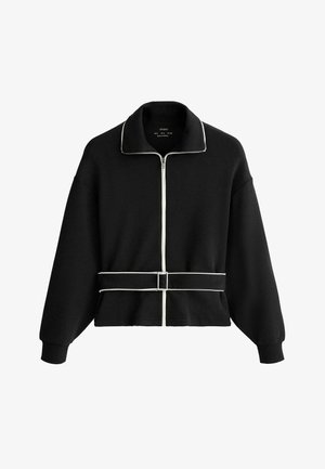 Zwarte lange mouwen ritsjas met witte biezen langs de rits, kraag en tailleband met gesp.