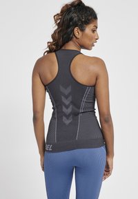 Svart atletisk linne med racerback-design. Har grå chevronmönster och ribbad textur, i kombination med blå ribbade leggings.