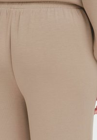 Beige leggings med en glat tekstur og elastisk talje, der fremhæver en tætsiddende silhuet og sømløst design.