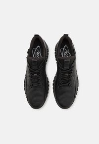 Musta urheilujalkine, jossa on teksturoitu verkkopintaosa, pehmustettu pohja ja rakenteellinen nauhakiristys. Varustettu kumipohjalla, jossa on pito kuvioita.