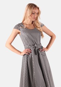 Schwarz-weiß kariertes Kleid mit kurzen Ärmeln, tailliertem Oberteil, Knoten-Detail an der Taille und schwingendem Rock. Aus Baumwollmaterial.