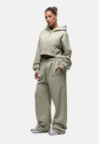 Felpa con cappuccio tagliata e pantaloni larghi in verde oliva tenue, caratterizzati da una vita elasticizzata e tasche laterali, con un delicato dettaglio di branding.