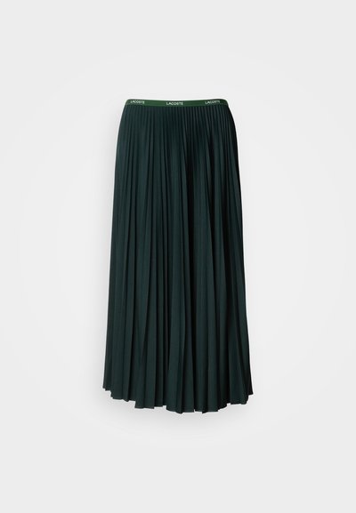 Jupe longue plissée de couleur vert foncé avec une large ceinture arborant le nom de la marque "LACOSTE" en lettres vertes contrastantes.