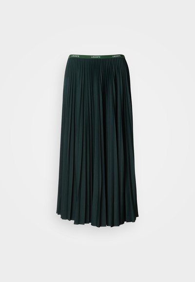 Jupe longue plissée de couleur vert foncé avec une large ceinture arborant le nom de la marque "LACOSTE" en lettres vertes contrastantes.