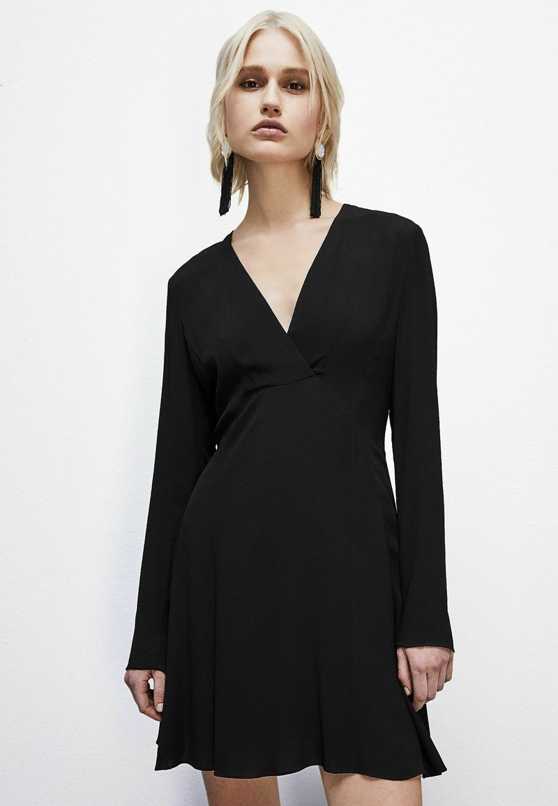 Schwarzes Langarmkleid mit tiefem V-Ausschnitt, tailliertem Oberteil und weit ausgestelltem Rock; glatte Textur und minimalistische Designmerkmale.