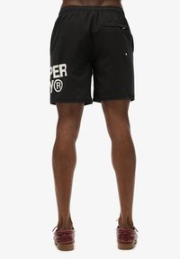 Zwarte zwemshorts met een verstelbare tailleband, voorzien van een wit logo op het linkerbeen en een achterzak met ritssluiting.