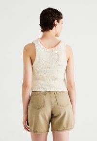 Gebreide mouwloze top in off-white met spikkels, voorzien van een perzikkleurige rand. Gemaakt in combinatie met lichtbeige, high-waisted denim shorts.