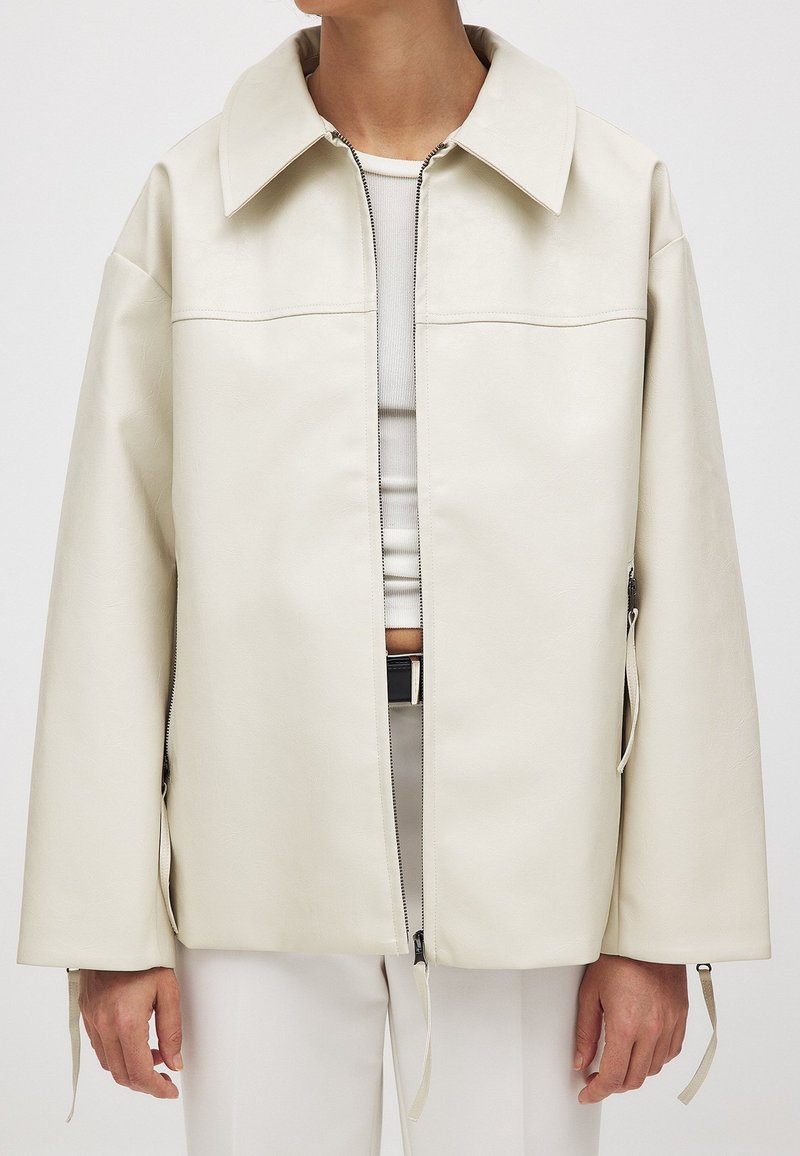 Kreminės odos striukė su priekine užtrauktuko uždarymo sistema, dideliu apykakle ir šoninėmis užtrauktukų detalėmis; pasižymi lygiu paviršiumi ir laisvu, kvadratiniu siluetu.