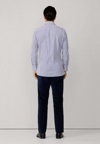 Blau-weiß gestreifte Button-up-Hemd mit Standardkragen, langen Ärmeln und taillierter Silhouette, kombiniert mit dunkelblauen Hosen.