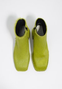 Botas de tobillo de pelaje sintético verde con una amplia punta cuadrada, cierre de cremallera lateral y textura suave, con un interior negro liso.