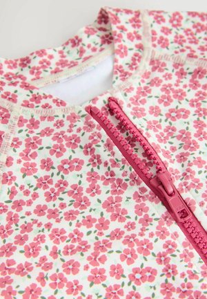 Floral-patterned fabric in pink and green hues, featuring a pink zipper at the neckline. Smooth texture with stitched seams.