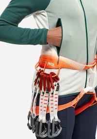 Harnais d'escalade en orange avec plusieurs points d'attache. Comprend des sangles grises et blanches avec des mousquetons. Porter avec un haut vert et blanc.