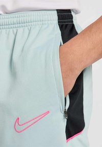 Svetlo modri športni kratki hlače z črnimi stranskimi paneli, z roza Nike логом, z žepi na zadrgo in mrežasto teksturo za zračnost.