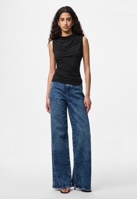 Μαύρο αμάνικο τοπ με σχέδιο σε draped ύφασμα, σε συνδυασμό με φαρδιά μπλε τζιν παντελόνια με ξεθωριασμένο πλύσιμο και φθαρμένες λεπτομέρειες στο τελείωμα.