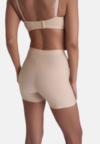 Beige sömlös bh med justerbara axelband och hyskförslutning, kombinerad med matchande högmidjade shorts, båda gjorda av ett mjukt och stretchigt material.