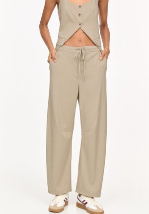 Pantalon large beige à fines rayures avec taille à cordon, porté avec un haut sans manches boutonné assorti et des baskets blanches.