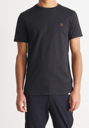 Uomo che indossa una maglietta nera semplice a maniche corte con piccolo logo arancione "II" sul petto sinistro, abbinata a pantaloni neri.