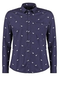 Chemise à manches longues bleu marine avec un petit motif d'oiseaux blancs et une poche poitrine sur le côté gauche.