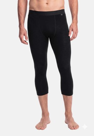 Homme portant des leggings noirs ajustés trois-quarts, debout pieds nus sur fond blanc, torse et bras visibles jusqu'au milieu de la poitrine.