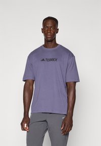 Fioletowa koszulka Adidas Terrex z krótkim rękawem i okrągłym dekoltem. Na przedzie znajduje się czarne logo. Miękka, lekka tkanina.