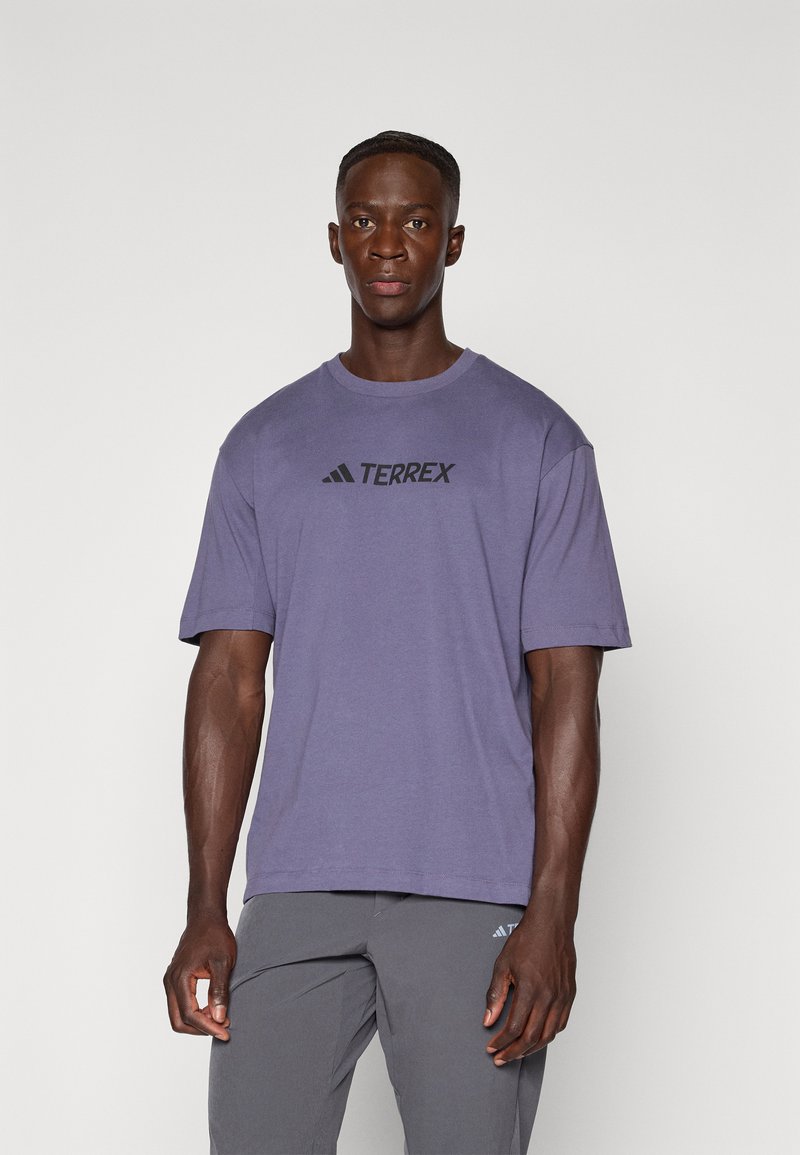 Fioletowa koszulka Adidas Terrex z krótkim rękawem i okrągłym dekoltem. Na przedzie znajduje się czarne logo. Miękka, lekka tkanina.