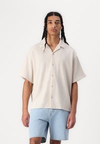 Cămașă cu mânecă scurtă, în dungi bej deschis, cu guler și cinci nasturi, asortată cu pantaloni scurți din denim albastru deschis.