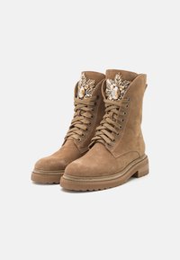 Botas de ante marrón con cordones que presentan adornos decorativos en la parte superior, una suela gruesa y costuras reforzadas a lo largo de la suela.