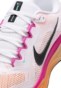 Sneakers marki Nike z białą siateczkową cholewką, różowymi akcentami, czarnym logo Swoosh oraz pomarańczową i różową teksturowaną podeszwą. Sznurowadła są białe.