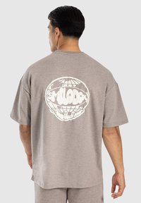 Grå bomulds t-shirt med korte ærmer, der har et stort hvidt grafik af hænder, der holder en globus på ryggen. Afslappet pasform.