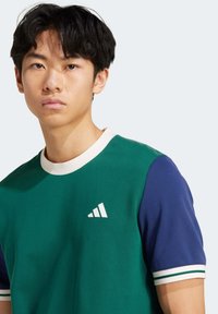 Green and navy short-sleeve shirt with a white crew neck, featuring a white logo on the chest and striped accents on the sleeves.