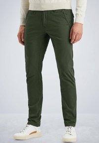 Mörkgröna bomullsbyxor med slim fit, med framfickor, tillsammans med vita sneakers med bruna detaljer.