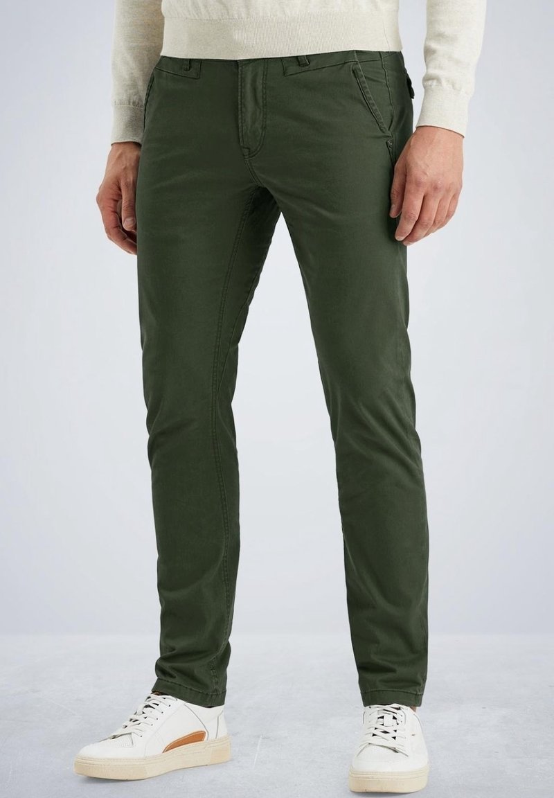 Mörkgröna bomullsbyxor med slim fit, med framfickor, tillsammans med vita sneakers med bruna detaljer.