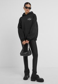 Felpa nera con il testo "Let's Get Lost", pantaloni neri aderenti, stivali platform neri spessi e una borsa a tracolla nera con manico intrecciato.