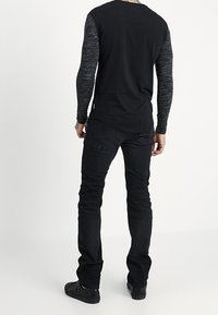 Svart långärmad tröja med grå texturerade ärmar och rund halsringning, kombinerad med svarta jeans och mörka skor.