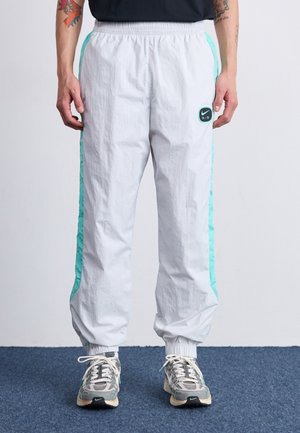 White lightweight pants with turquoise side stripes, elastic waistband, and ankle cuffs. Includes a small black Nike logo on the left thigh.