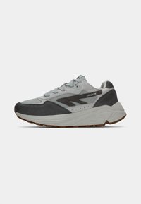 Sneaker grise avec un mélange de matériaux en suède et en maille, présentant un logo noir proéminent, des détails texturés et une semelle légère et courbée.