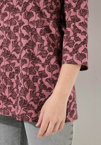 Top rosa con un motivo a foglie nere, scollo rotondo e maniche a tre quarti. Tessuto morbido con un aspetto leggermente strutturato.