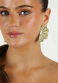 Guldörhängen med ett fläktformat design, som har texturerade ytor och glittrande accenter, som fångar ljus mot en neutral bakgrund.