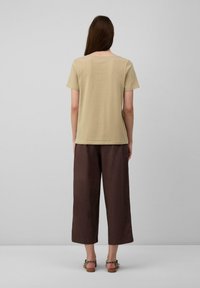 Beige T-Shirt mit kurzen Ärmeln, kombiniert mit lockeren, braunen, weiten Hosen und braunen Sandalen. Angenehme Textur, lässiger Schnitt und schlichtes Design.