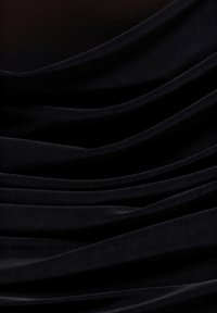 Musta kangas, jossa on pehmeä, laskostettu tekstuuri ja kevyt kiilto. Sileä pinta ja pyöristetyt reunat luovat elegantteja laskoksia kauttaaltaan.