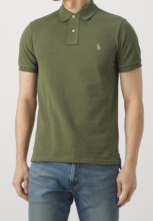 Oliven grøn polo shirt i blød bomuld, korte ærmer, tre-knaps placket og broderet logo på venstre bryst. Kombination med blå jeans.