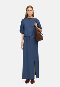 Niebieski, fakturowany dwuczęściowy zestaw składający się z luźnej bluzki i długiej spódnicy z bocznym rozcięciem. Akcesoria to brązowa torebka z zamszu i czerwone buty.