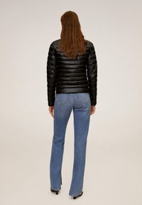 Sort puffet jakke med horisontal syning, parret med lysblå flarejeans. Jakken har en ståkrave og en skinnende finish.