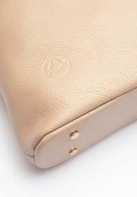 Borsa in pelle beige con superficie testurizzata, dotata di un logo impresso e due borchie dorate sulla parte inferiore per stabilità.