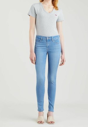Camiseta gris de cuello en V con un pequeño logotipo, combinada con jeans ajustados de color azul claro. Los jeans cuentan con un diseño clásico de cinco bolsillos y un sutil desgastado.