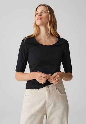 Schwarzes, tailliertes T-Shirt mit rundem Halsausschnitt und Ärmel in Ellenbogenlänge, kombiniert mit hellen, hoch-taillierten Jeans.