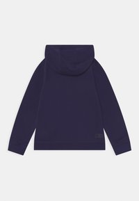 Sudadera azul marino con capucha ajustable, mangas largas y dobladillo acanalado. Presenta un pequeño parche de logo negro en el lado inferior. Textura suave.